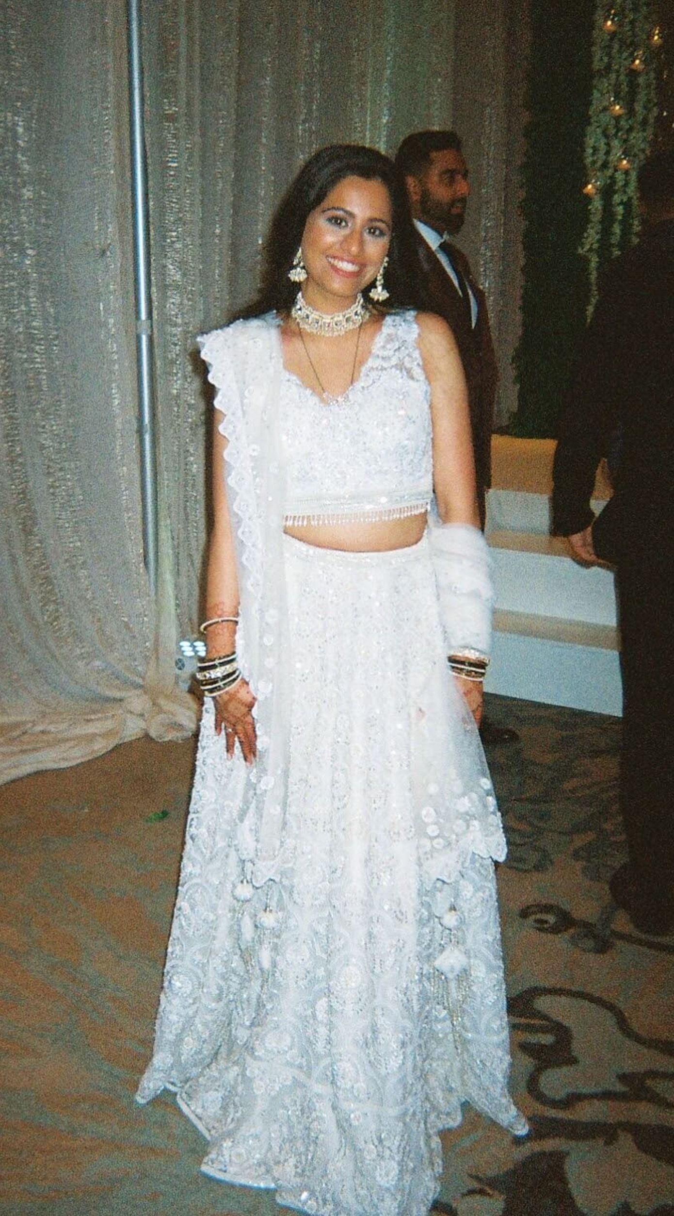 The Rucha Lehenga is a white hand-embroidered lehenga adorned with Swarovski crystals. It features a v-neck blouse with two tie details in the back. It comes with a completely detachable can-can.