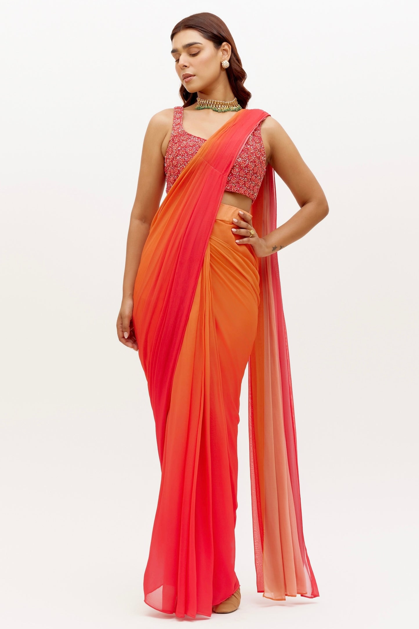 The Mirai Drape Saree showcases a printed ombre skirt with an attached drape that's paired with a hand-embroidered blouse adorned with pearl and sequin detailing. The back of the blouse has beaded tassels for added fun.