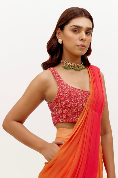 The Mirai Drape Saree showcases a printed ombre skirt with an attached drape that's paired with a hand-embroidered blouse adorned with pearl and sequin detailing. The back of the blouse has beaded tassels for added fun.