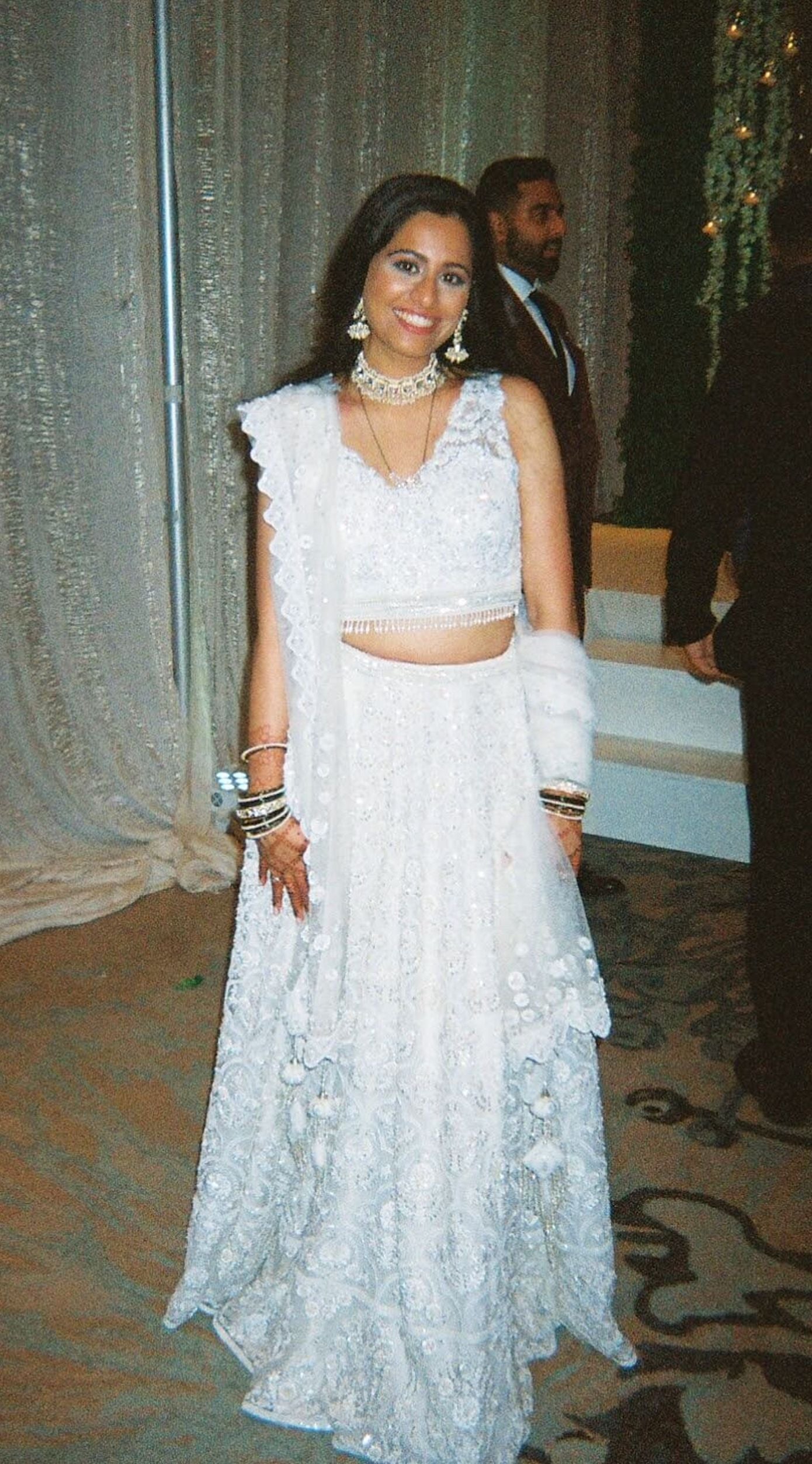 The Rucha Lehenga is a white hand-embroidered lehenga adorned with Swarovski crystals. It features a v-neck blouse with two tie details in the back. It comes with a completely detachable can-can. 