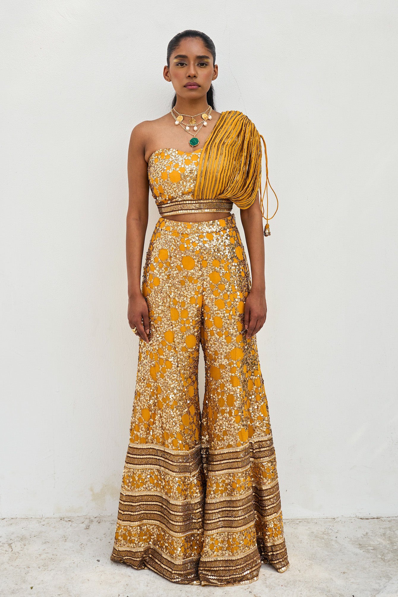 The sequined Tanvi Palazzo Set consists of a one-shoulder adjustable top and flared palazzo pants.